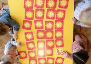 Dzieci siedzą wokół stołu, na którym rozłożone są kartoniki do gry w memory.